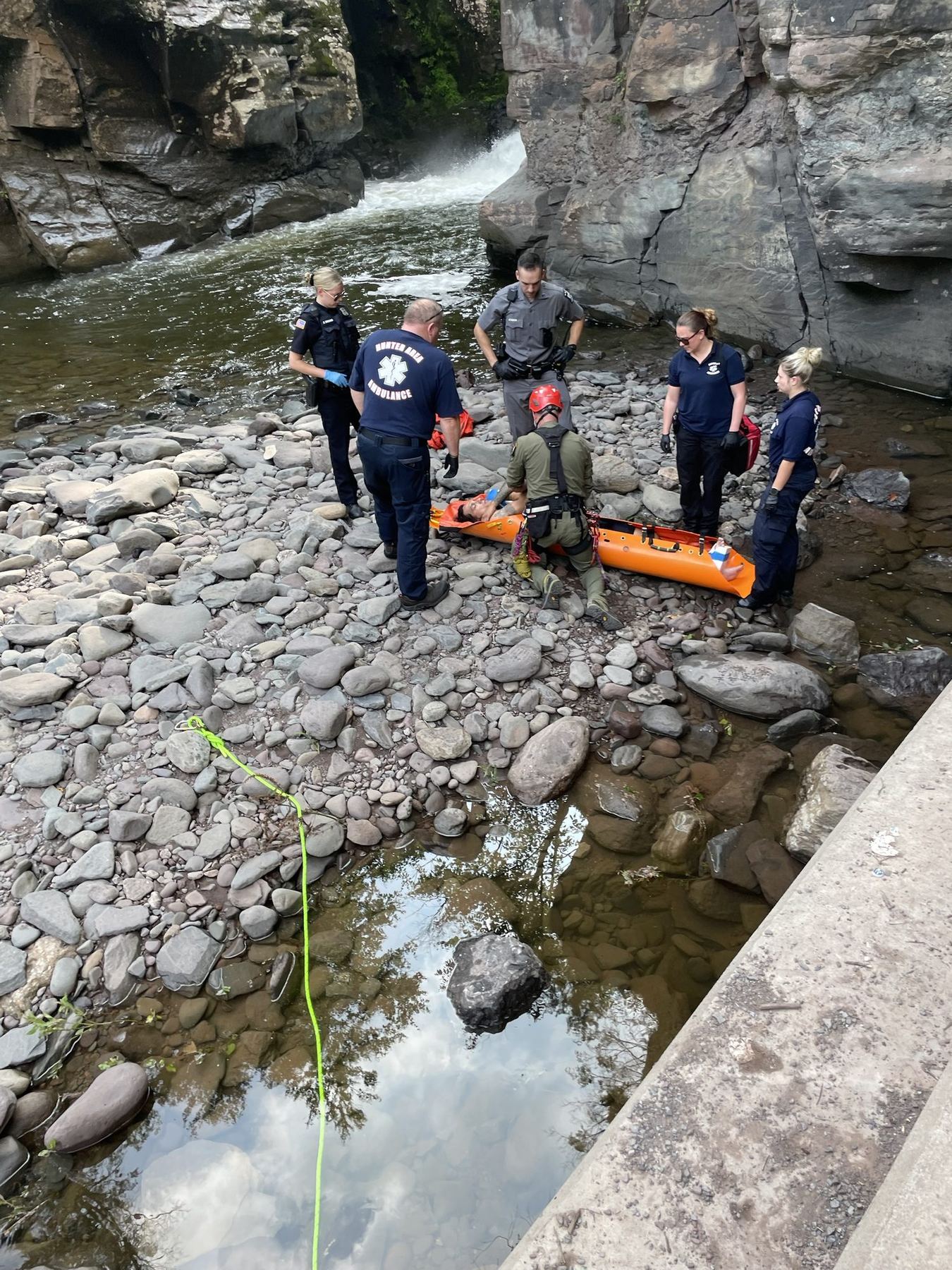 Rescue crews with a Greene County paramedic packaging a patient in a litter on a rocky creek bed beneath a waterfall