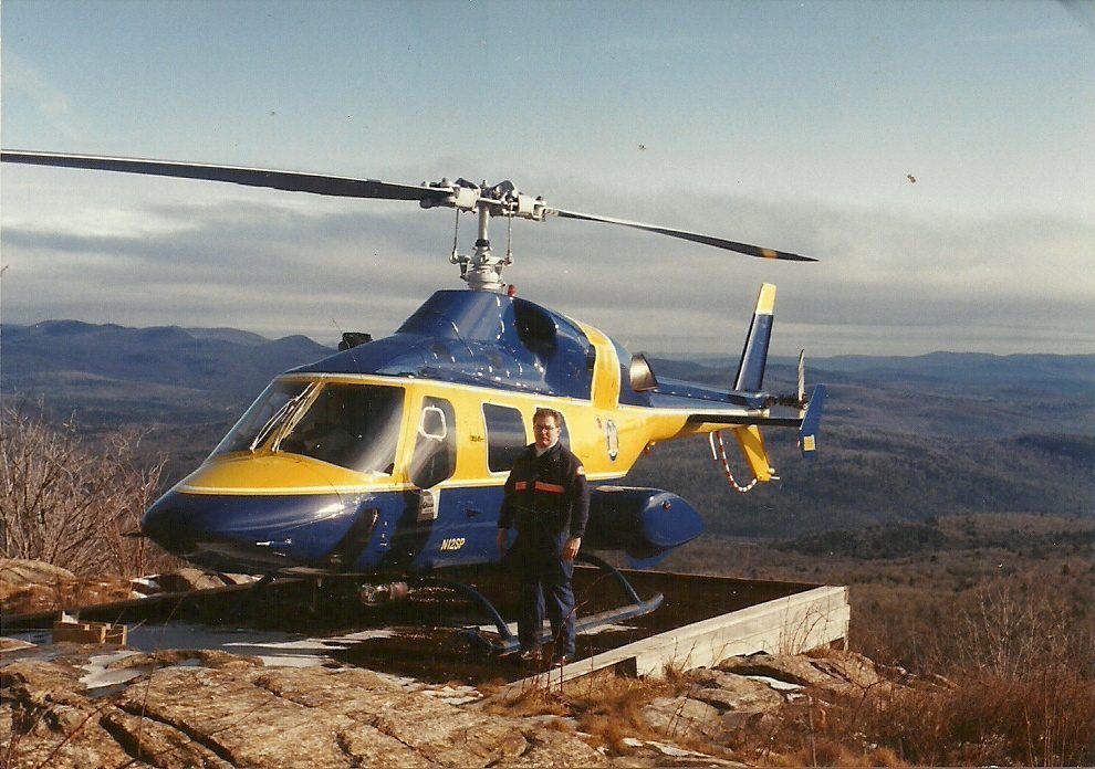 A flight paramedic beside a medical helicopter on a mountaintop landing pad