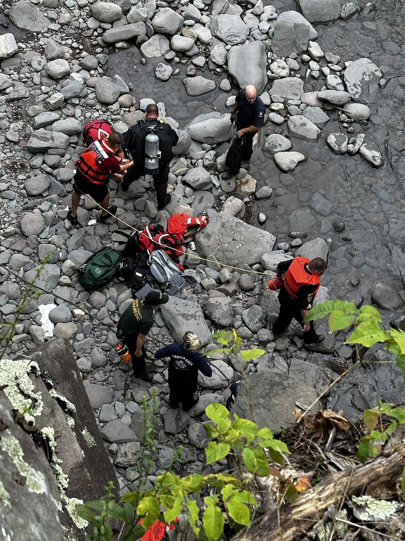 Rescuers, a diver and a Greene County paramedic working a swift-water scene on a rocky creek bed, seen from above