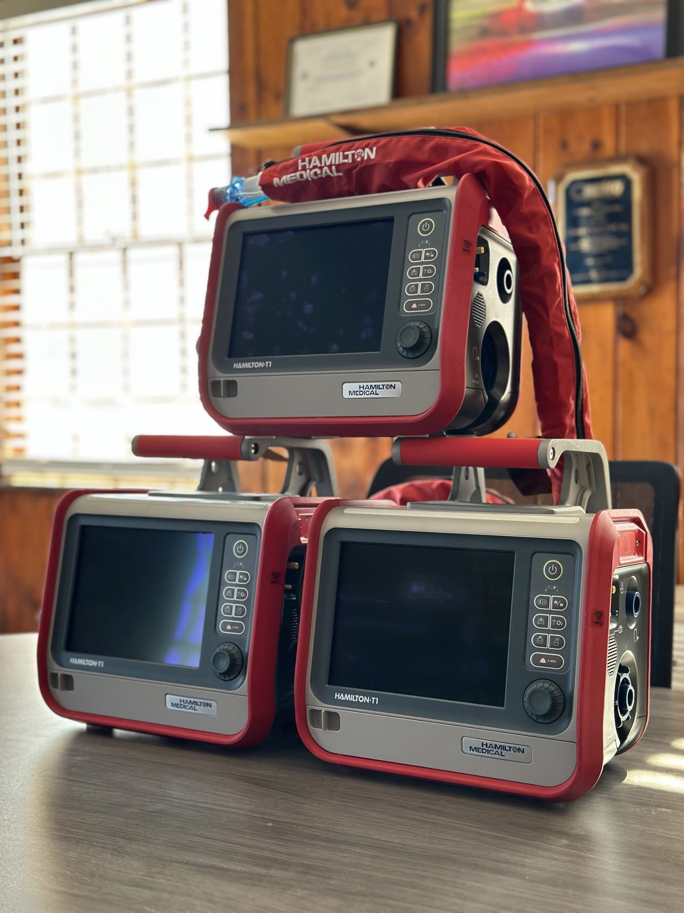Three Hamilton T1 ventilators stacked on a desk